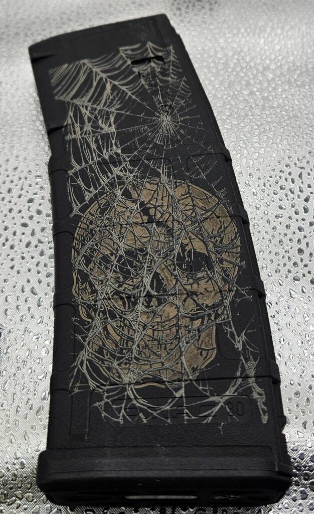 Detailed skull and spiderweb artwork laser-engraved on a polymer AR-15 magazine by Odell Arms